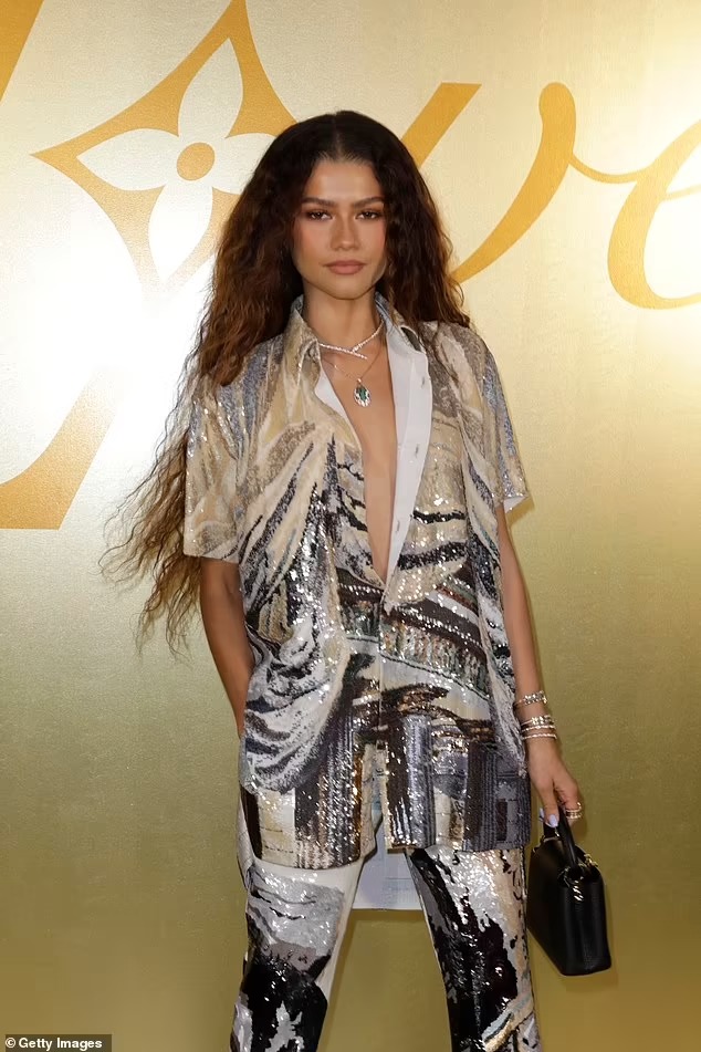 Zendaya commands attention as she goes braless in a shimmering gold patterned suit for Louis Vuitton’s Paris Fashion Week show