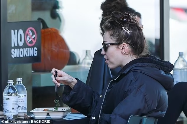 Miley Cyrus bundles up in a black billowy jacket as she enjoys lunch at upscale supermarket Erewhon in LA